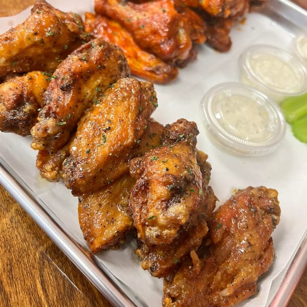 Sauce Wing Co. wings, some with red sauce and some with black pepper seasoning, with dipping sauces.