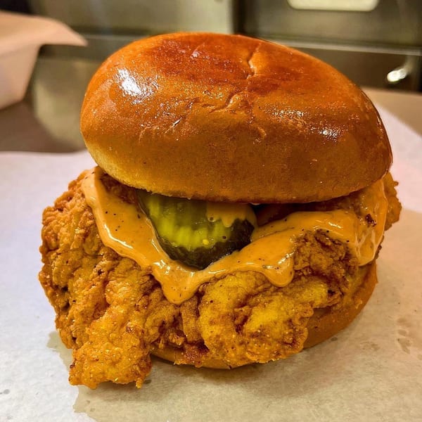 Crispy fried chicken sandwich with sauce and pickles on a brioche bun from Sauce Wing Co.
