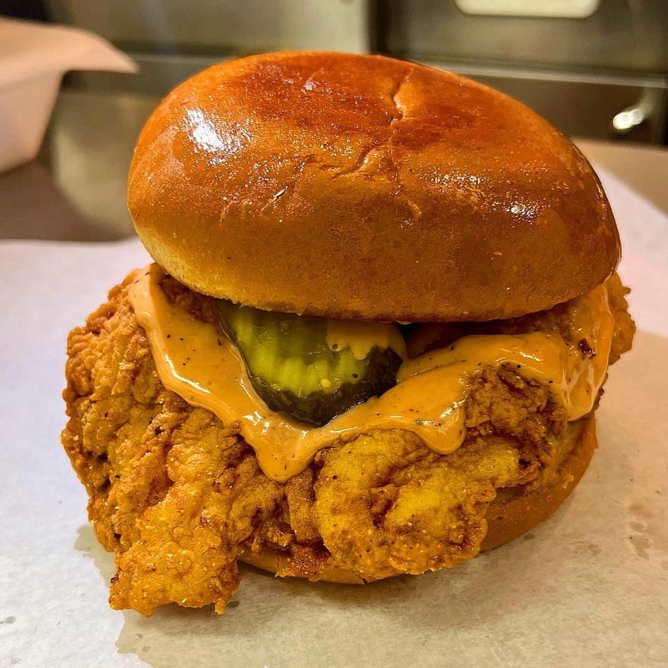 Crispy fried chicken sandwich with sauce and pickles on a brioche bun from Sauce Wing Co.