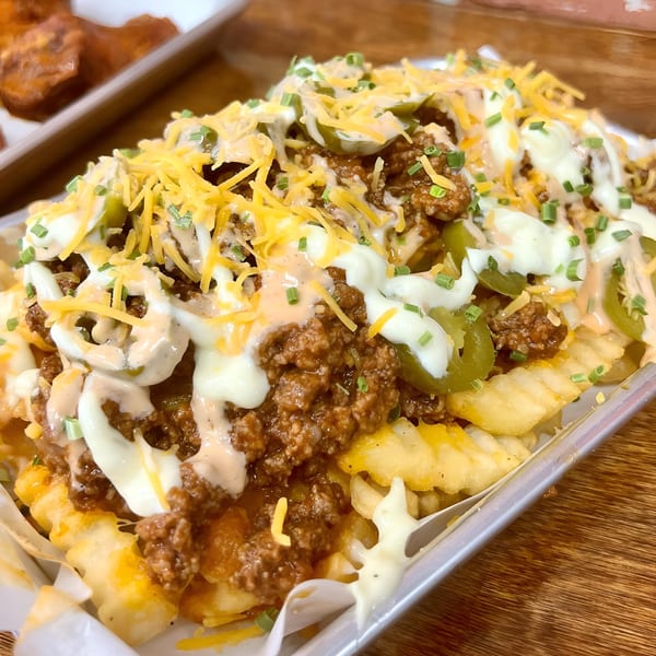 Sauce Wing Co's chili cheese fries with jalapeños, sour cream, and chives in a metal tray.
