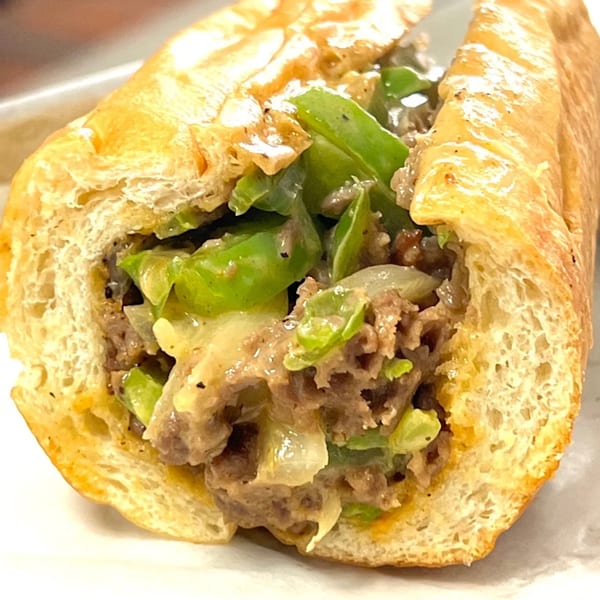 Close-up of a cheesesteak sandwich with steak, melted cheese, green peppers, and onions on a hoagie roll.