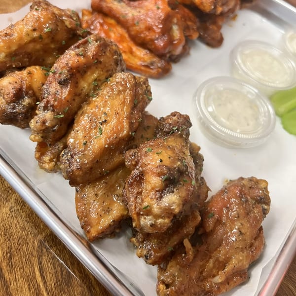 A tray of Sauce Wing Co's garlic parmesan and buffalo wings with dipping sauces and celery.