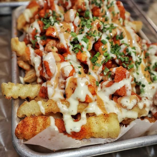 Sauce Wing Co's loaded fries with buffalo chicken, ranch, and chives in a metal tray.