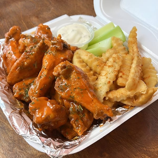 Sauce Wing Co. buffalo wings with crinkle-cut fries, celery sticks, and ranch dressing in a takeout container.