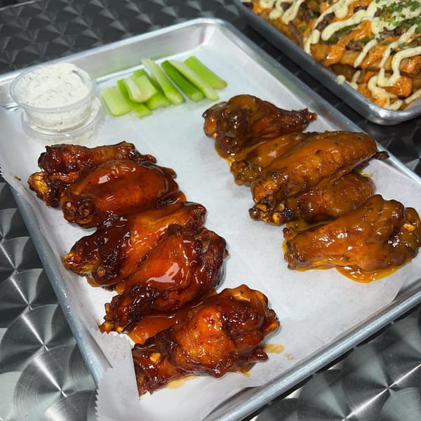 Two rows of Sauce Wing Co. wings, one with dark sauce and one with lighter sauce, with celery and ranch.